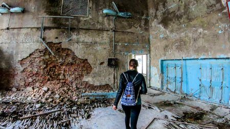 Girl in black outfit walks around the rotten floor in an abandoned sports hall in Pripyat, Ukraine, after the Chernobyl explosion.