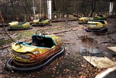 Old broken rusty metal radioactive yellow cars, electric cars for children, abandoned among vegetation, culture and recreation park in Pripyat city, Chernobyl disaster, Ukraine.
