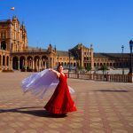 Flamenco dancer in red dress dancing with spanish shawl on Plaza de Espana in Seville, Spain