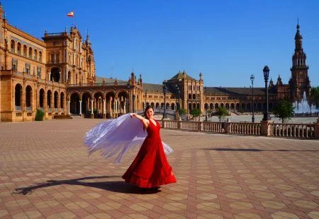Flamenco dancer in red dress dancing with spanish shawl on Plaza de Espana in Seville, Spain