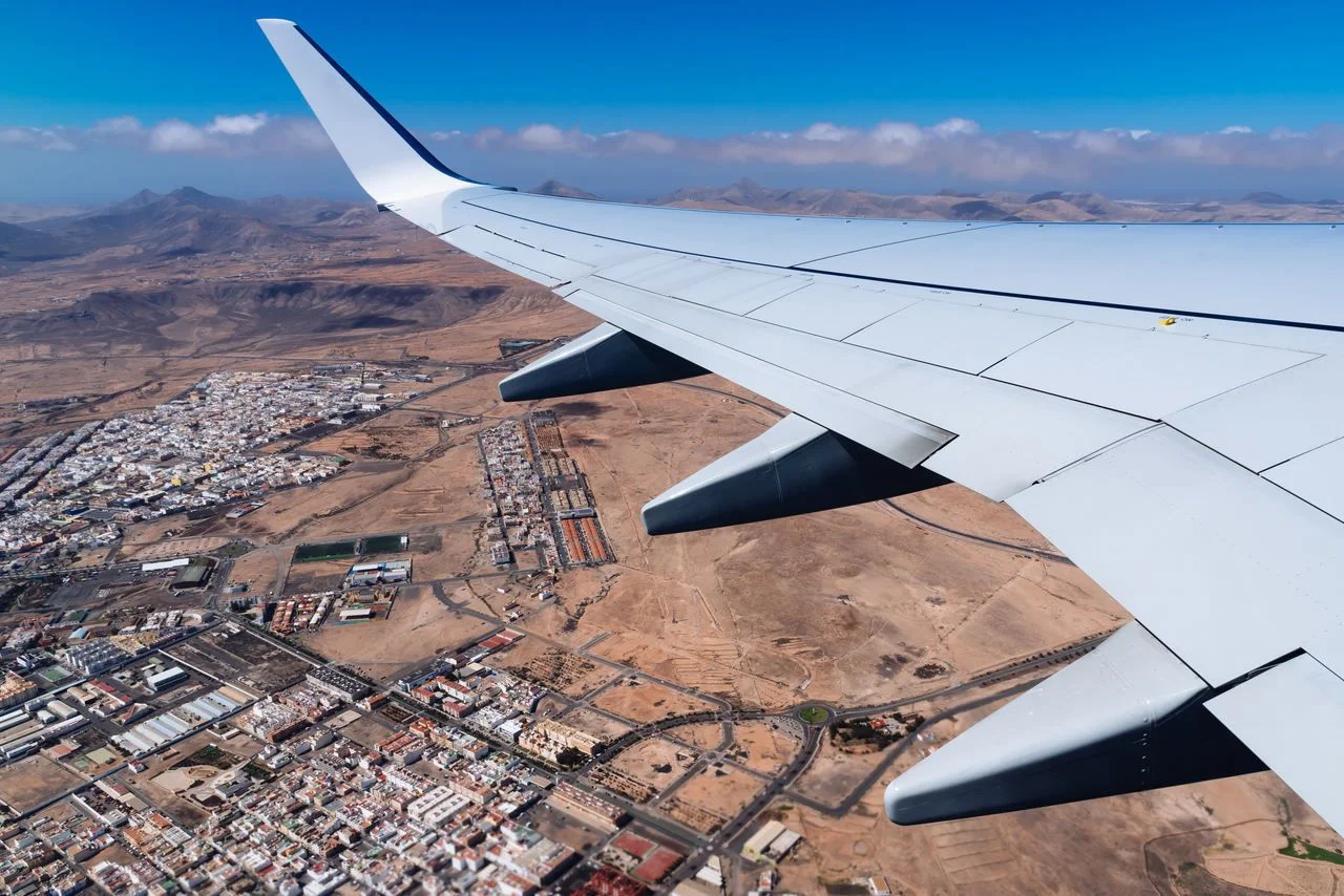 Wing of airplane taking off Fuerteventura Airport, above city.