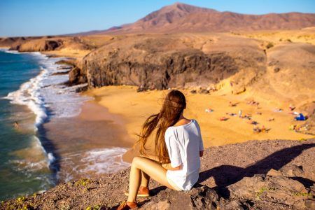 Young female tourist sitting and enjoying beautiful view on Papagayo beach on Lanzarote