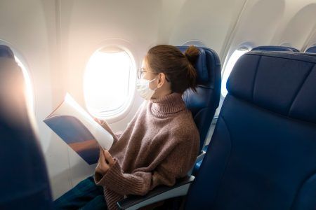 A young woman wearing face mask is traveling on airplane