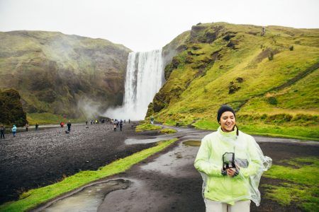 Excited tourist woman sightseeing at popular Icelandic location. Visiting Skogafoss waterfall.