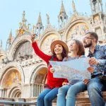 Group of happy friends travelers with map on San Marco Square in Venice. Vacation and holidays in Italy and Europe concept