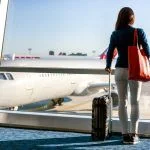 Tourist traveling while standing with his luggage watching the sunset at the airport window. Airport transfers.