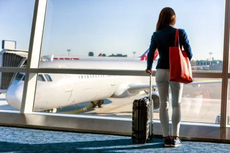 Tourist traveling while standing with his luggage watching the sunset at the airport window. Airport transfers.