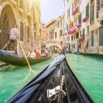 Traditional gondolas on a narrow canal in Venice, Italy with retro vintage toned Instagram style grunge filter and lenses flare sunlight effect on a sunny day with blue skies in summer