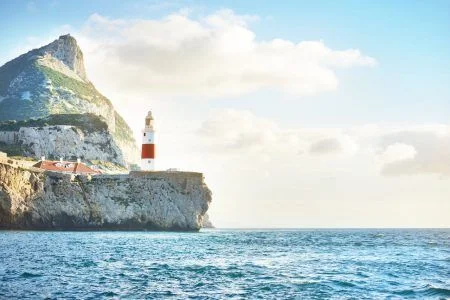 Trinity lighthouse at the rocky shore (cliffs) of the Europa Point. British Overseas Territory of Gibraltar, Mediterranean sea. Epic cloudscape. National landmark, sightseeing, travel destination