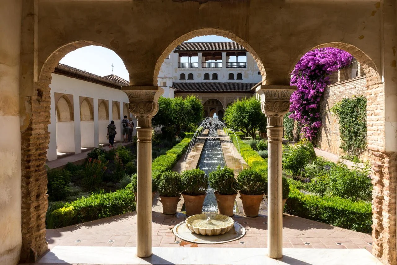 View of The Generalife courtyard, with its famous fountain and garden through an arch. Alhambra de Granada complex at Granada, Spain, Europe on a bright summer day