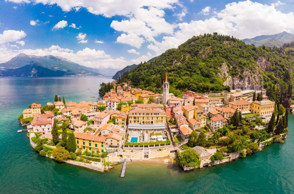 Beautifull aerial panoramic view from the drone to the Varenna – famous old Italy town on bank of Como lake. High top view to Water landscape with green hills, mountains and city in sunny summer day.