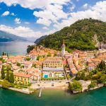 Beautifull aerial panoramic view from the drone to the Varenna – famous old Italy town on bank of Como lake. High top view to Water landscape with green hills, mountains and city in sunny summer day.
