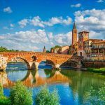 Panoramic view of the Ponte Pietra bridge in Verona on the Adige river. Veneto region. Italy. Sunny summer day panorama and blue dramatic sky with clouds. Ancient European Italian terracotta color ho