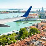 Plane flies above Venice, Italy. Aerial panoramic view of city and sea from airplane window. The plane’s wing over Venice during taking off or landing. Concept of flight, vacation and summer travel.