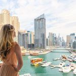 Woman in Dubai Marina, United Arab Emirates. Attractive lady wearing a long dress admiring Marina harbor daylight view