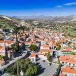 Aerial bird’s eye view of Kalavasos village valley, Larnaca, Cyprus. A traditional town with ceramic roof tiles houses, a greek orthodox christian church and muslim mosque around hills from above.