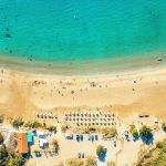 Aerial view of Coral Bay beach – popular beach with clear sea water and comfortable sandy beach, many tourists, sunbeds with umbrellas in Peyia village, Cyprus.