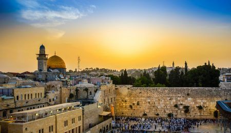 Jewish people gather for Shacharit sunrise prayer at the WesternWailing Wall, the holiest place in Judaism, with the muslim Dome of the Rock, the Temple Mount and Mount of Olives in the background
