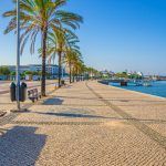 Ribeirinha de Portimao town, cobblestone embankment promenade of Arade River in city centre with palm trees and benches, blue sky background, Faro district, Algarve region, Portugal