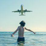 Teen boy in the wave of the sea on the beach in the headphones under the landing planes in Laranca