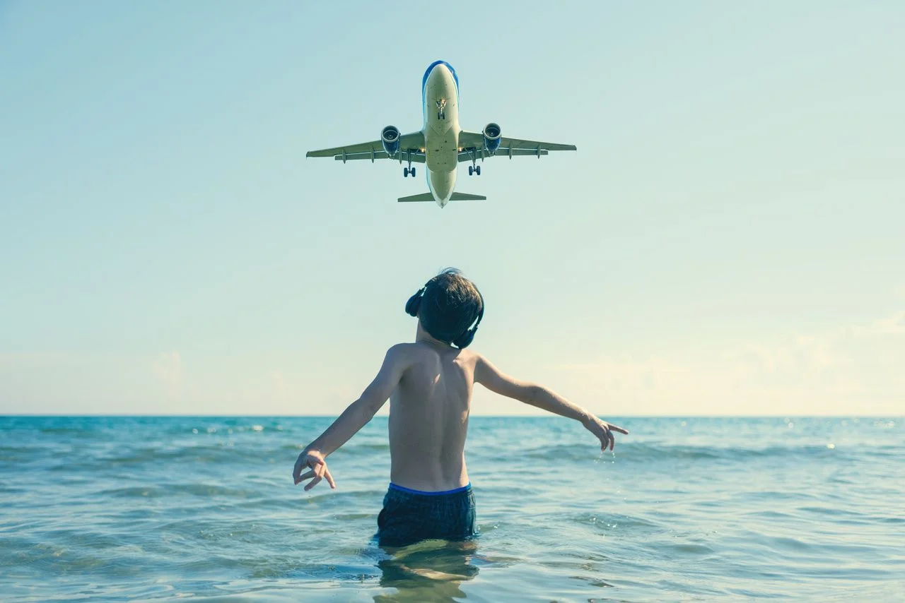 Teen boy in the wave of the sea on the beach in the headphones under the landing planes in Laranca