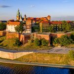 Krakow, Poland. Wawel Hill, royal Cathedral and castle. Aerial view in sunset light. Vistula River and far view of St. Mary (Mariacki) church on the left. Riverbank with promenade and walking people.