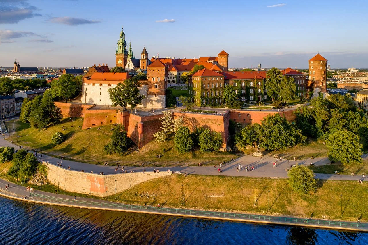 Krakow, Poland. Wawel Hill, royal Cathedral and castle. Aerial view in sunset light. Vistula River and far view of St. Mary (Mariacki) church on the left. Riverbank with promenade and walking people.