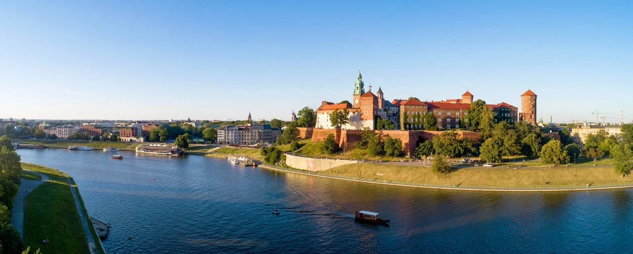 Krakow, Poland. Wide aerial panorama at sunset with Royal Wawel castle and cathedral. Vistula river banks, tourist boats, parks, promenades and walking people