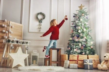 Cute little child girl is decorating the Christmas tree indoors.