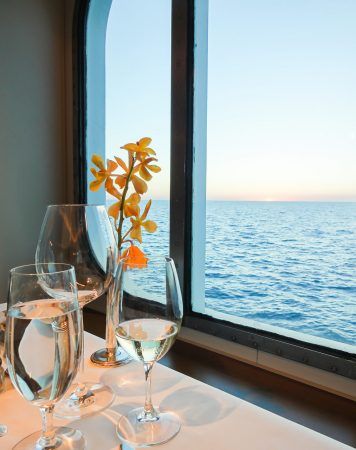Table dinner setting with flower, wine and water glasses. Ocean background.