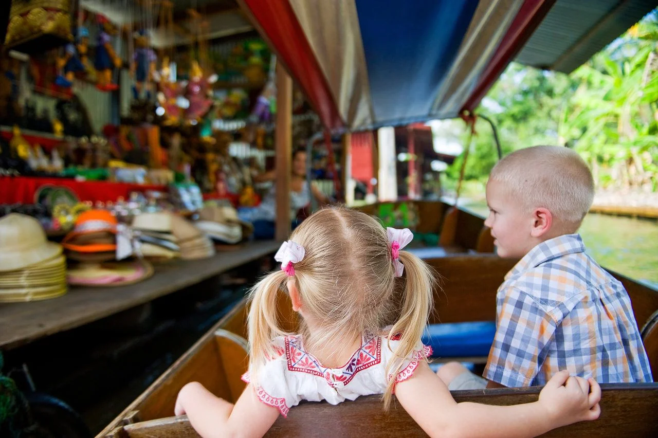 Two caucasian kids enjoy traveling on boat at Damnoen Saduak floating market, Thailand