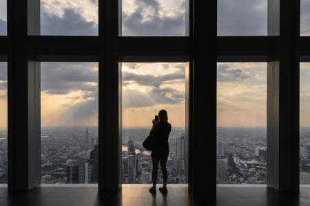 Woman sightseeing the city on top of bangkok building through windows at sunset