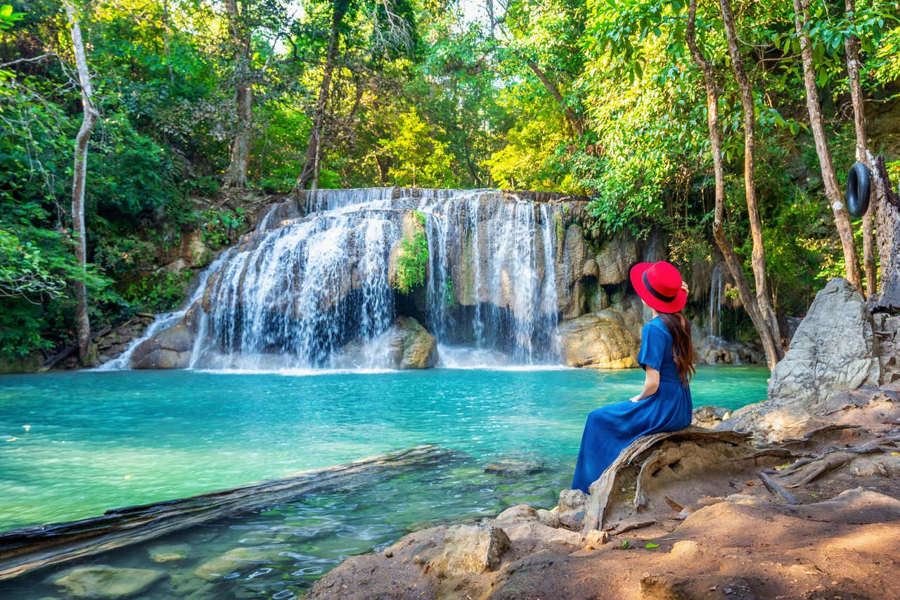Woman sitting at Erawan waterfall in Thailand. Beautiful waterfall with emerald pool in nature.