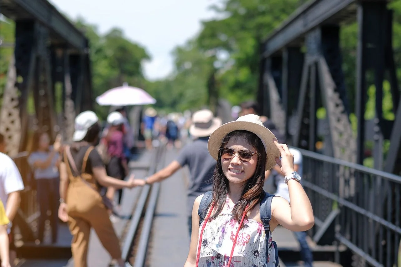 Young Woman traveling backpacker with hat, Asian traveler standing on the railway bridge over the river Kwai in Kanchanaburi, Thailand