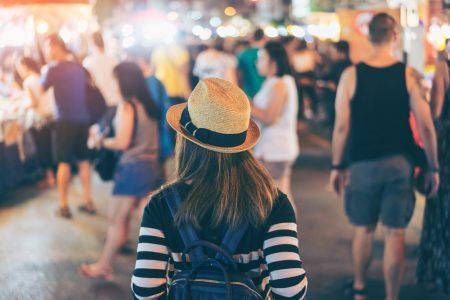 Young asian woman traveler backpacker with hat and bag traveling to Chiang Mai night walk street market at Chiang Mai Province, Thailand.