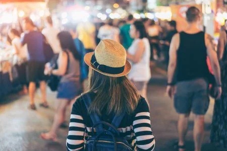 Young asian woman traveler backpacker with hat and bag traveling to Chiang Mai night walk street market at Chiang Mai Province, Thailand.