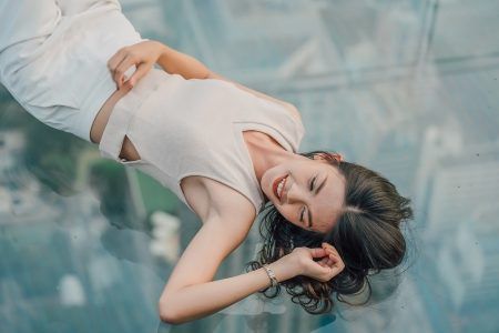 Young asian woman traveler enjoying and posing on glass floor on rooftop of the King Power Mahanakhon building high above Bangkok