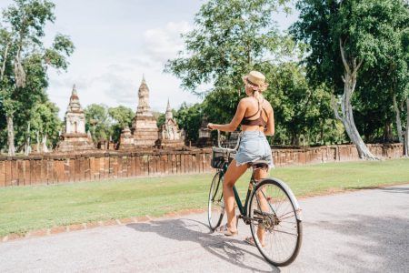 Young blonde woman riding a bicycle looking architecture in nature, in Sukhotai Thailand