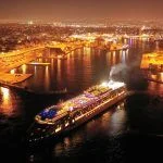 Aerial drone night shot of beautiful illuminated port of Piraeus and huge cruise liner departing to Aegean popular destinations, Attica, Greece