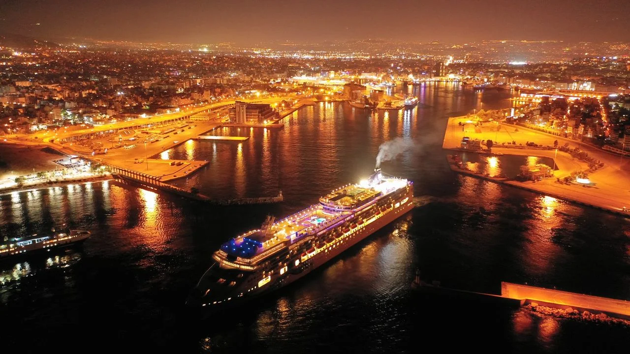 Aerial drone night shot of beautiful illuminated port of Piraeus and huge cruise liner departing to Aegean popular destinations, Attica, Greece
