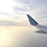 Airplane wing flying above white clouds obscure light from the sun. View from aircraft window.