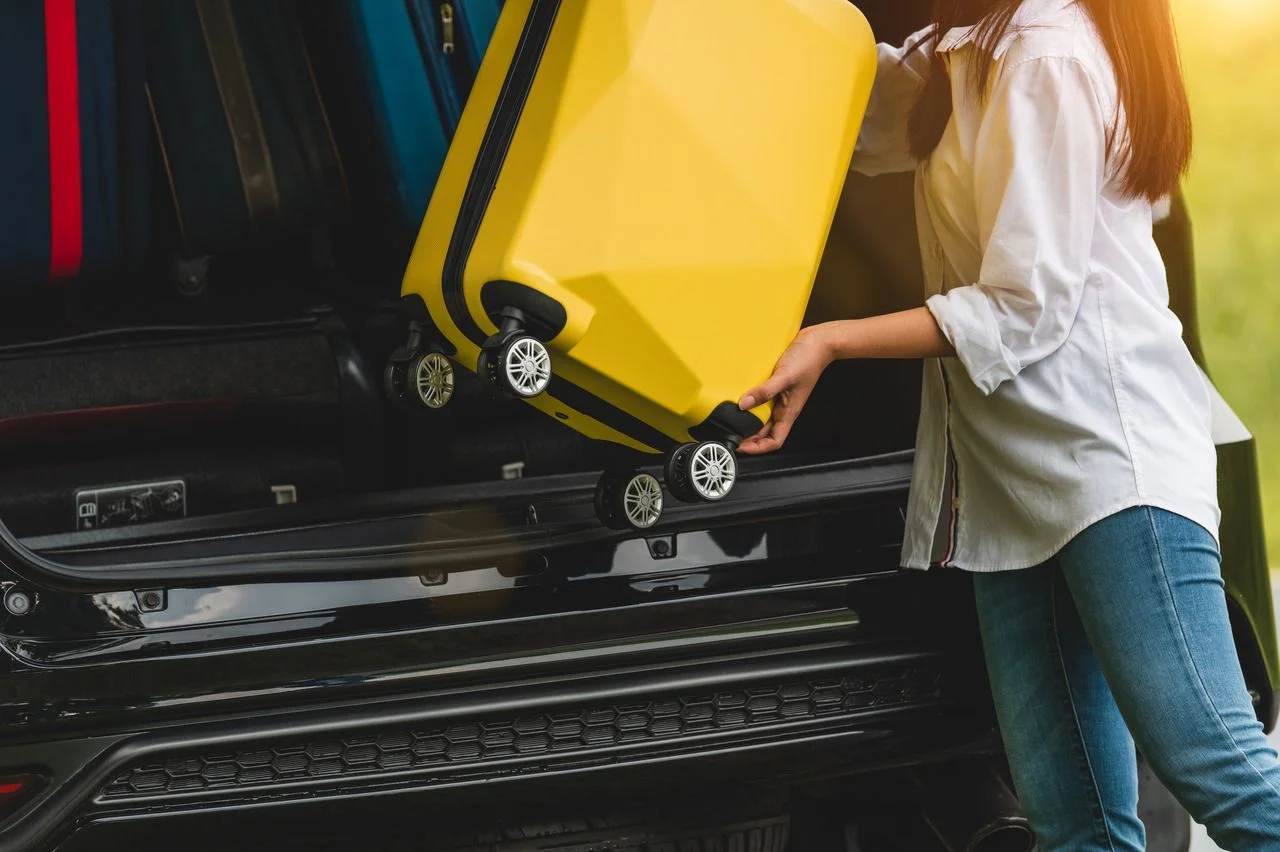 Asiain woman lifting yellow suitcase into SUV car during travel in long weekend trip. People lifestyles and transportation