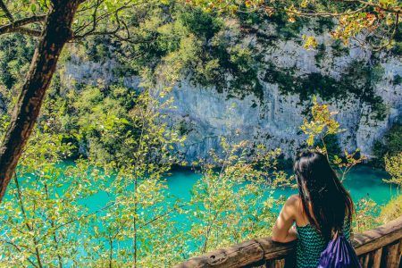 Back view of young woman looking at a stunning lake with turquoise water in Plitvice Lakes National Park, Croatia.