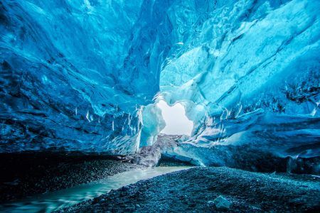 Blue crystal ice cave entrance and underground river below a glacier in Iceland