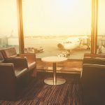 Departure lounge at the airport with seating and table with planes preparing for flight in the background