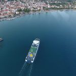 Drone shot of a ferry with yellow circle at the top dock sailing towards the port of Astakos, West Greece