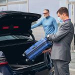 Serious elegant dark-haired Caucasian airport driver putting his client traveling bag in the car trunk