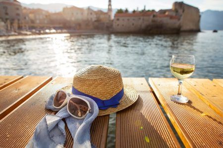 A straw hat, glasses and a glass of wine stands on a pier near the sea, close-up. Selective focus, noise. Beautiful light from the sun. Place for text