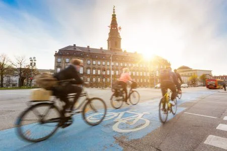 Blurred people riding a bicycle in Copenhagen, with Christiansborg Palace in the background. Many people prefer to cycle rather than take a car or bus to get around the city. Urban lifestyle concept.