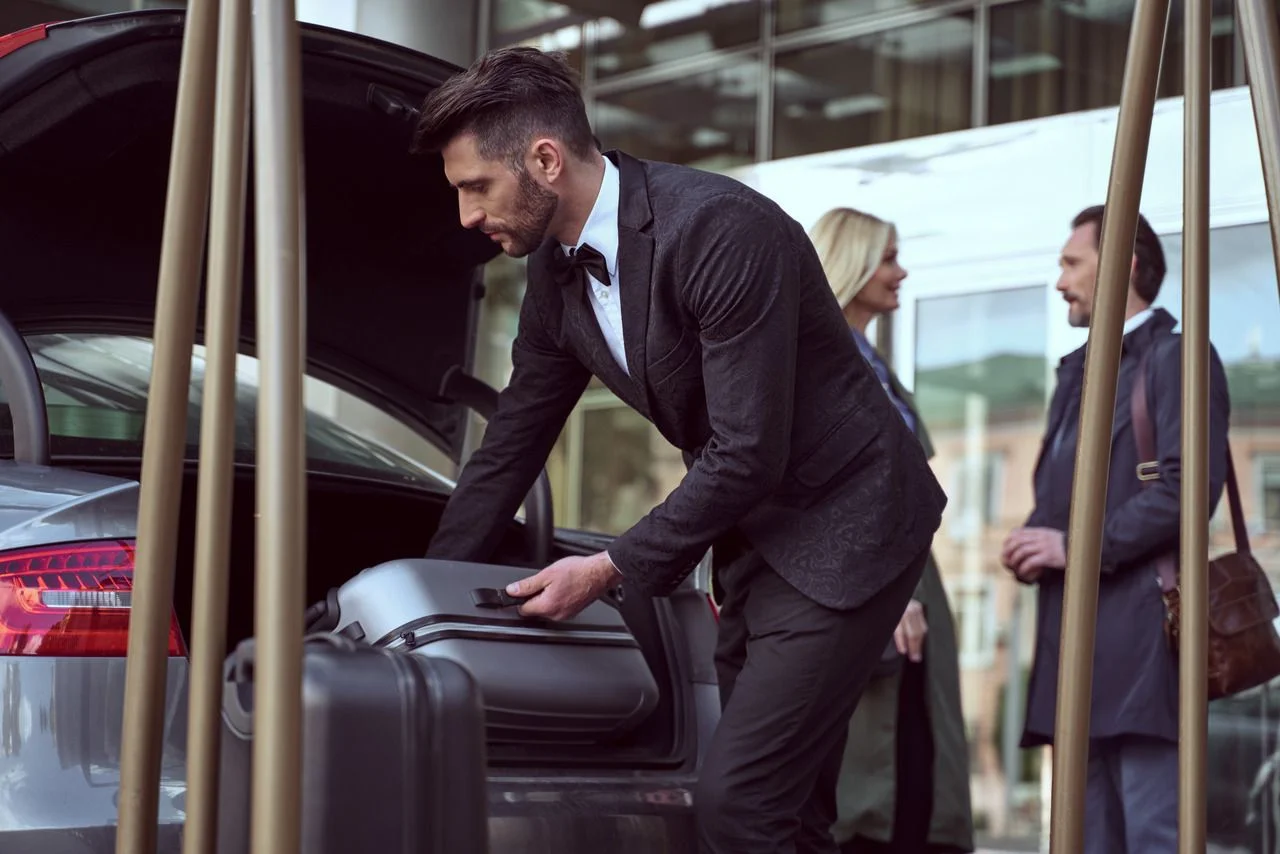 Dedicated hotel employee satnding near the open car trunk taking out a suitcase helping the guests with luggage